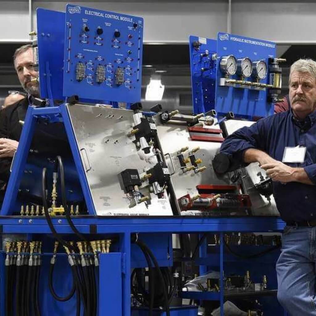 People stand among some of the trainers for electronics, hydraulics, pnuematics, and mechanics while listening to one of the speakers during the ribbon cutting ceremony at the new Three Rivers Community College Manufacturing Apprenticeship Center at Grasso Tech in Groton on Tuesday, Nov. 19, 2019. (Dana Jenson/The Day)